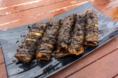 Atıştırmalık olarak eritilmiş çikolatalı kızarmış muz. Tabakta kızarmış muz ruloları..