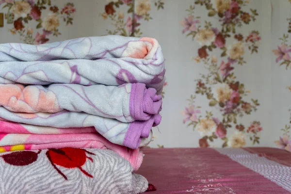 White folded duvet lying. Stacked of colorful blanket on pink bed. Folded pink blankets