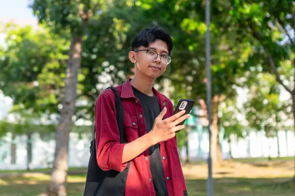 スマートフォンを使ってカメラを探している若いアジアの大学生 パブリックパークの男子生徒 コピースペース — ストック写真