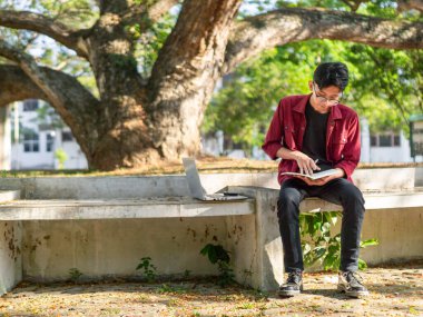 Asyalı üniversite öğrencisi kampüs parkında kitap okuyor.. 