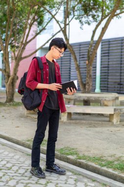 Asyalı üniversite öğrencisi kampüs parkında kitap okuyor.. 