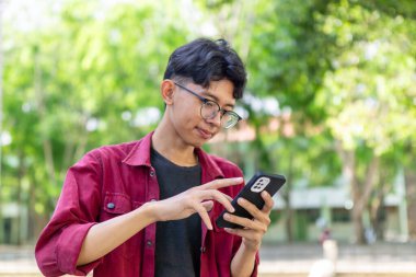Telefonunu tutarken gülümseyen Asyalı bir adamın portresi. Kırmızı gömlekli adam akıllı telefon kullanırken kameraya neşeyle gülümsüyor.