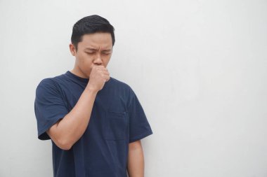 Genç Asyalı adam beyaz üzerine öksürüyor. Soğuk algınlığı belirtileri gösteren bir adam. Sağlıklı konsept.