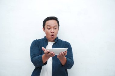 Elinde mutlu ve heyecanlı bir ifadeyle boş bir tabak tutarken mavi gömlek giyen mutlu Asyalı bir adamın portresi. Genç adam boş model plakayı gösteriyor ve işaret ediyor. Beyaz arkaplan ile izole edilmiş.