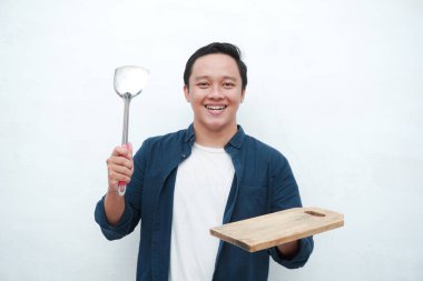 Mutlu Asyalı bir adamın mutlu ve heyecanlı bir ifadeyle boş bir kesiği tutarken portresi. Genç adam boş tahta kesme tahtasını gösteriyor ve işaret ediyor. Beyaz arkaplan ile izole edilmiş.