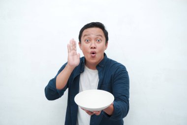 Elinde mutlu ve heyecanlı bir ifadeyle boş bir tabak tutarken mavi gömlek giyen mutlu Asyalı bir adamın portresi. Genç adam boş model plakayı gösteriyor ve işaret ediyor. Beyaz arkaplan ile izole edilmiş.