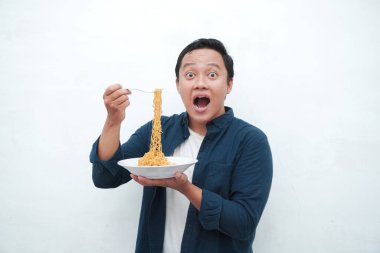 Mavi tişörtlü mutlu Asyalı bir adamın portresi. Bir tabak kızarmış erişte yemek için heyecanlı. Gülümseyen ve elinde bir tabak erişte tutan genç adam. Beyaz arkaplan ile izole edilmiş.