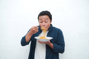 Mavi tişörtlü mutlu Asyalı bir adamın portresi. Bir tabak kızarmış erişte yemek için heyecanlı. Gülümseyen ve elinde bir tabak erişte tutan genç adam. Beyaz arkaplan ile izole edilmiş.