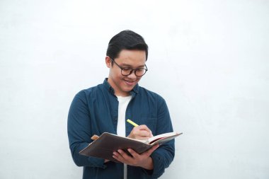 Genç Asyalı adam düşünürken ve konsantre olurken kitapları tutuyor. Beyaz arkaplan üzerinde çalışırken Asyalı öğrenci fikir arıyor