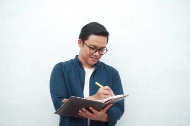 Genç Asyalı adam düşünürken ve konsantre olurken kitapları tutuyor. Beyaz arkaplan üzerinde çalışırken Asyalı öğrenci fikir arıyor