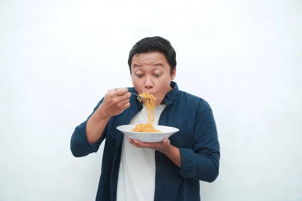 stock image A portrait of happy Asian man wearing a blue shirt excited to eat a plate of fried noodles. Young man smiling and holding a plate of noodle. Isolated with a white background.