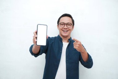 Mutlu Asyalı adam elinde mutlu ve heyecanlı bir ifadeyle boş bir akıllı telefon ekranı tutuyor. Mavi tişörtlü, gülümseyen ve reklam için beyaz cep telefonu ekranı gösteren genç bir Asyalı..