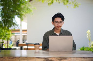 Dışarıdaki kafede dizüstü bilgisayarda çalışan Asyalı bir adam. Bilgisayarda bir fincan kahveyle çalışan bir adam..
