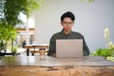 Dışarıdaki kafede dizüstü bilgisayarda çalışan Asyalı bir adam. Bilgisayarda bir fincan kahveyle çalışan bir adam..