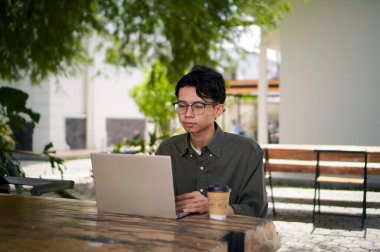 Dışarıdaki kafede dizüstü bilgisayarda çalışan Asyalı bir adam. Bilgisayarda bir fincan kahveyle çalışan bir adam..
