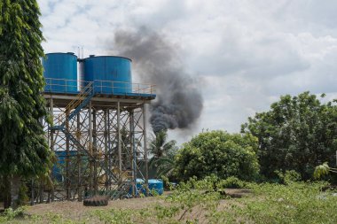 Industrial factory pollution from palm oil factory in Indonesia. Smoke coming out of the chimneys at the sunny day clipart