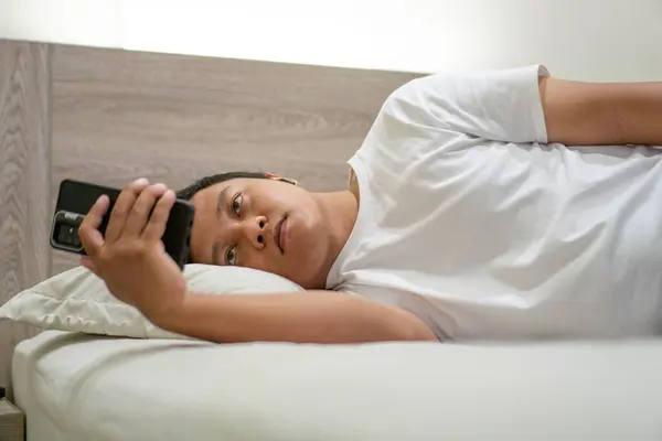 Geceleri yatakta akıllı telefon kullanan bir adam. Genç Asyalı adam akıllı telefon kullanırken yatakta yatıyor. Kötü alışkanlık.