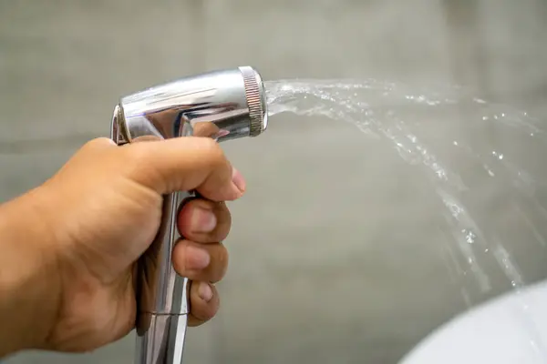Erkek el, tuvalette durulama spreyi hortumunu tutuyor. Banyoda el yapımı bidet. Krom bide duşu tuvalette tutarken elinizi kapatın..