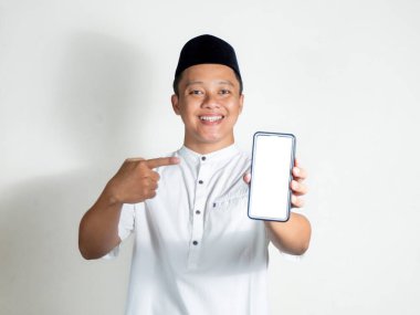 Müslüman Asyalı adamın portresi gülümsüyor ve akıllı telefon boş ekranı gösteriyor. Müslüman beyaz gömlekli ve siyah şapkalı.