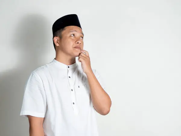 Müslüman Asyalı adam düşünüyor ve konsantre oluyor. Beyaz arka planda fikirler ararken çenesini tutan bir adam.