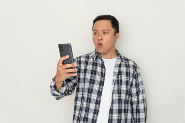 Genç Asyalı adam korkmuş ve şaşırmış bir ifadeyle cep telefonunu işaret ediyor. Promosyon ve kötü haber kavramı
