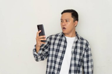 Genç Asyalı adam korkmuş ve şaşırmış bir ifadeyle cep telefonunu işaret ediyor. Promosyon ve kötü haber kavramı