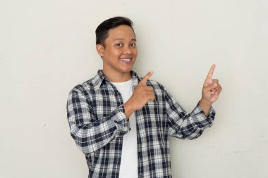 Çekici genç Asyalı adam gülümsüyor ve parmağını yana doğrultuyor. Boşluğu kopyala. 