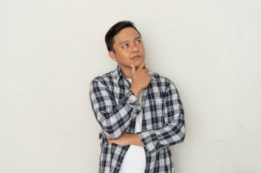 Genç Asyalı adam düşünüyor, konsantre oluyor ve çenesini tutuyor. Asyalı öğrenci beyaz arkaplan üzerinde düşünüyor ve fikirler arıyor