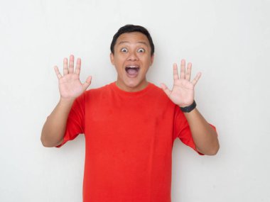 Şaşırmış ve heyecanlı bir ifadesi olan genç Asyalı bir adam, elleri havada ve ağzı beyaz arka planda açık. Kırmızı gömlekli adam şaşırmış görünüyor.