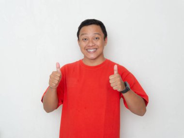 Kırmızı tişörtlü genç Asyalı adam beyaz arka planda güvenle gülümsüyor. Pozitiflik, onay ve memnuniyet kavramı