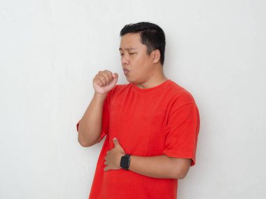 Kırmızı gömlekli genç Asyalı adam eline öksürüyor. Beyaz arka planda öksüren akıllı bir adam. Soğuk semptomlar