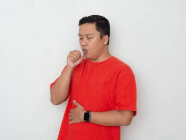 Kırmızı gömlekli genç Asyalı adam eline öksürüyor. Beyaz arka planda öksüren akıllı bir adam. Soğuk semptomlar