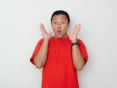 Şaşırmış ve heyecanlı bir ifadesi olan genç Asyalı bir adam, elleri havada ve ağzı beyaz arka planda açık. Kırmızı gömlekli adam şaşırmış görünüyor.