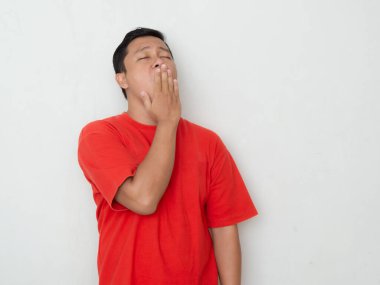 Kırmızı gömlekli genç Asyalı adam eli ağzında esniyor. Kırmızı gömlekli adam uykulu, sağlıklı konsept