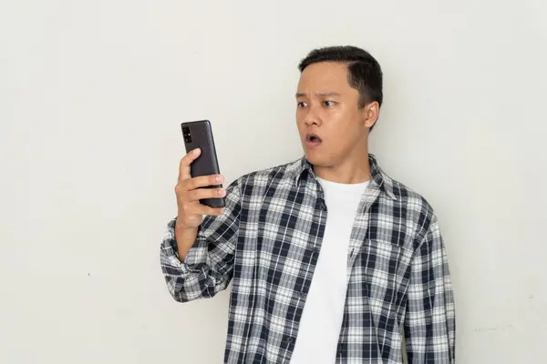 Genç Asyalı adam korkmuş ve şaşırmış bir ifadeyle cep telefonunu işaret ediyor. Promosyon ve kötü haber kavramı