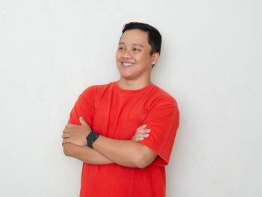 Kırmızı tişörtlü gülümseyen Asyalı genç adam, kollarını kavuşturmuş beyaz arka planda duruyor..