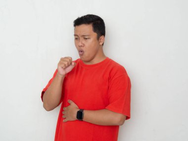 Kırmızı gömlekli genç Asyalı adam eline öksürüyor. Beyaz arka planda öksüren akıllı bir adam. Soğuk semptomlar