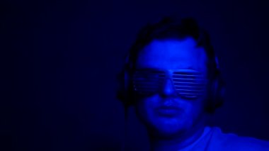 Kulaklıklı bir adam renkli, yanıp sönen neon renkte müzik dinliyor. Gece kulübünde şık bir genç adam. Ağır çekimde siyah arka planda kulaklık takan DJ..