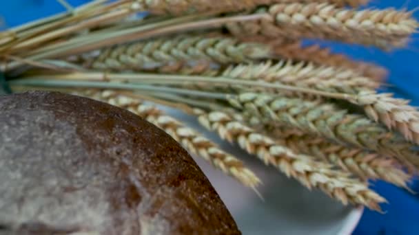天然焼きたての自家製パンは 小麦のスパイクレットと木製のテーブルの上に スローモーションパン — ストック動画
