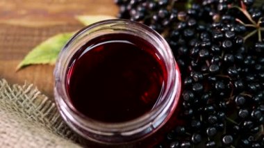 Cam bir kavanozda Doğal Yaşlı Meyve Suyu. Ahşap bir arka planda siyah mürver. Bitkisel ilaçlar. Homeopati, eski bir masada kara dut.