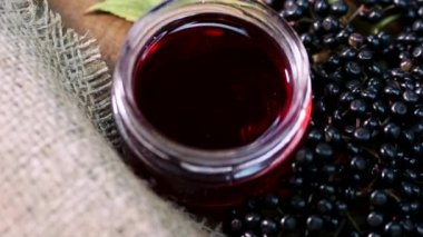 Ağır çekimde en üst görüntü. Cam kavanozda doğal elder çileği suyu. Ahşap bir arka planda siyah mürver. Bitkisel ilaçlar. Homeopati, eski bir masada böğürtlen. Mürver dalı
