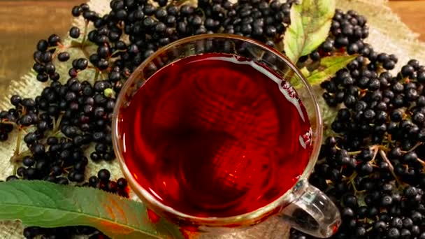 上からの眺めターンテーブルの上のガラスカップに天然の赤いベリーティー ブラックエルダーベリーのベリーティー ホメオパシージュースから圧迫ベリーサンブカスニングラ — ストック動画