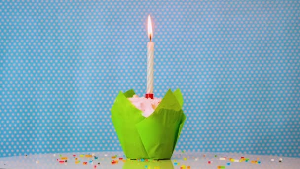 青い背景に燃えるろうそくと緑のお祝いマフィンのクローズアップ あらゆる年齢のための幸せな誕生日の背景 クリームマフィンだ 創立記念事業 — ストック動画