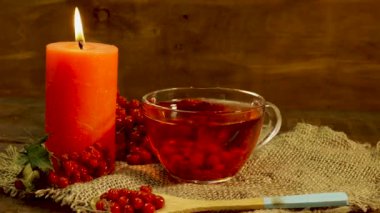 Tahtadaki kırmızı viburnum böğürtleninden yakın plan kırmızı çay. Böğürtlene dayalı sağlıklı naturopati ya da homeopati için güzel kokulu çay. Mum yanıyordu, masada çay vardı.