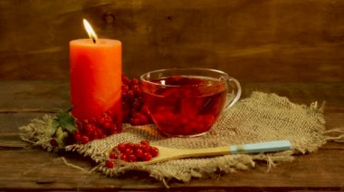 Ahşap bir masada, yanan bir mum ve kırmızı viburum meyveli kırmızı çay. Naturopati içeceği. Sağlıklı dolaşım sistemi için çay.