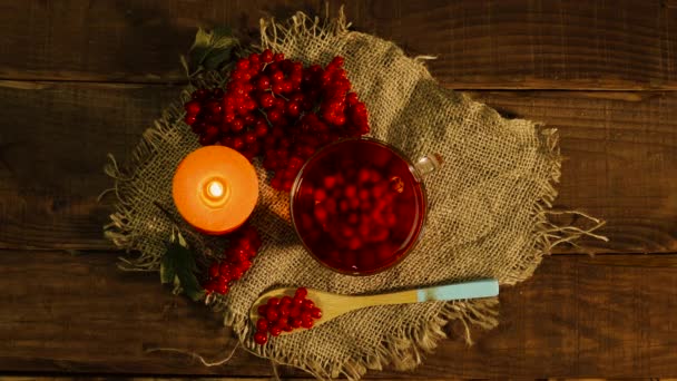 野焼きのキャンドルと赤いビブラムベリーのある木製のテーブルの上で天然の赤いお茶をお楽しみください 自然の同情を飲む 健康な循環器系のための茶 — ストック動画