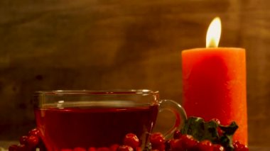 Yanan bir mum ve kırmızı viburnum çileği olan ahşap bir masada duran doğal kırmızı çay. Naturopati içeceği. Sağlıklı dolaşım sistemi için çay..