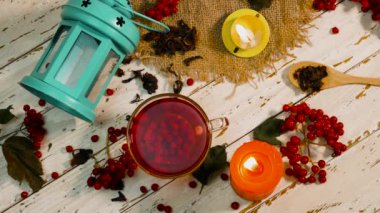 Beyaz ahşap bir masada kırmızı çay ve yanan mumlarla dolu bir fincanın arka planı. Kırsal panolardaki kırmızı viburnum üzümünün doğal çayı. Naturopati iyileşme aşısı. Antioksidan içeceği.