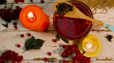 Beyaz ahşap bir masada kırmızı çay ve yanan mumlarla dolu bir fincanın arka planı. Kırsal panolardaki kırmızı viburnum üzümünün doğal çayı. Naturopati iyileşme aşısı. Doğal antioksidan içeceği.
