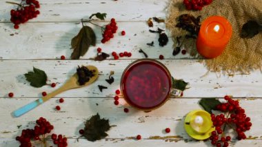 Beyaz ahşap bir masada kırmızı çay ve yanan mumlarla dolu bir fincanın arka planı. Kırsal panolardaki kırmızı viburnum üzümünün doğal çayı. Naturopati. Antioksidan içeceği..